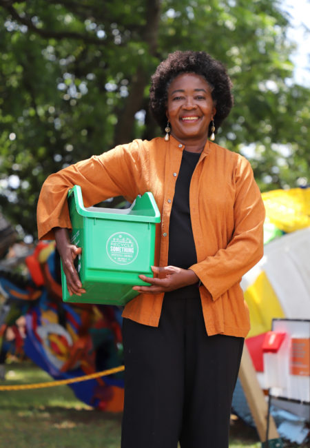 Smiling woman standing in front of trees with container under her right arm