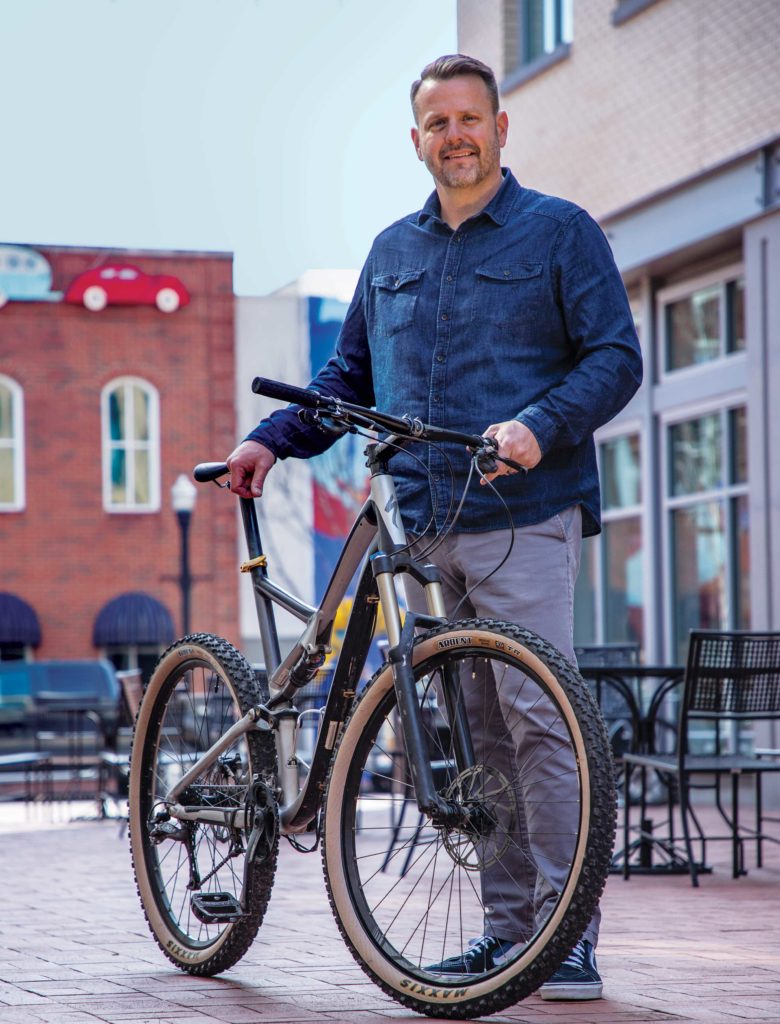 Ryan Hale poses with his mountain bike in an outdoor cafe area in downtown Bentonville, Arkansas