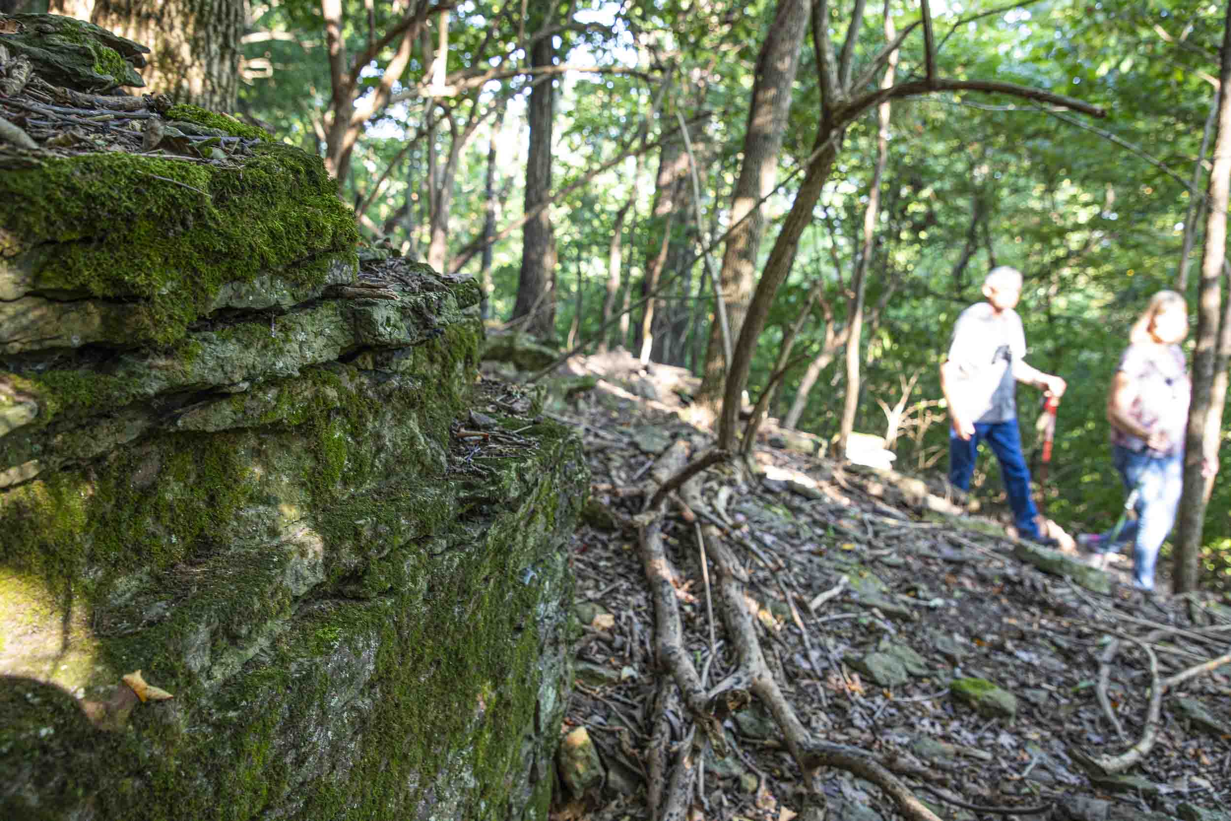 Hikers walk past a mossy rock outcropping