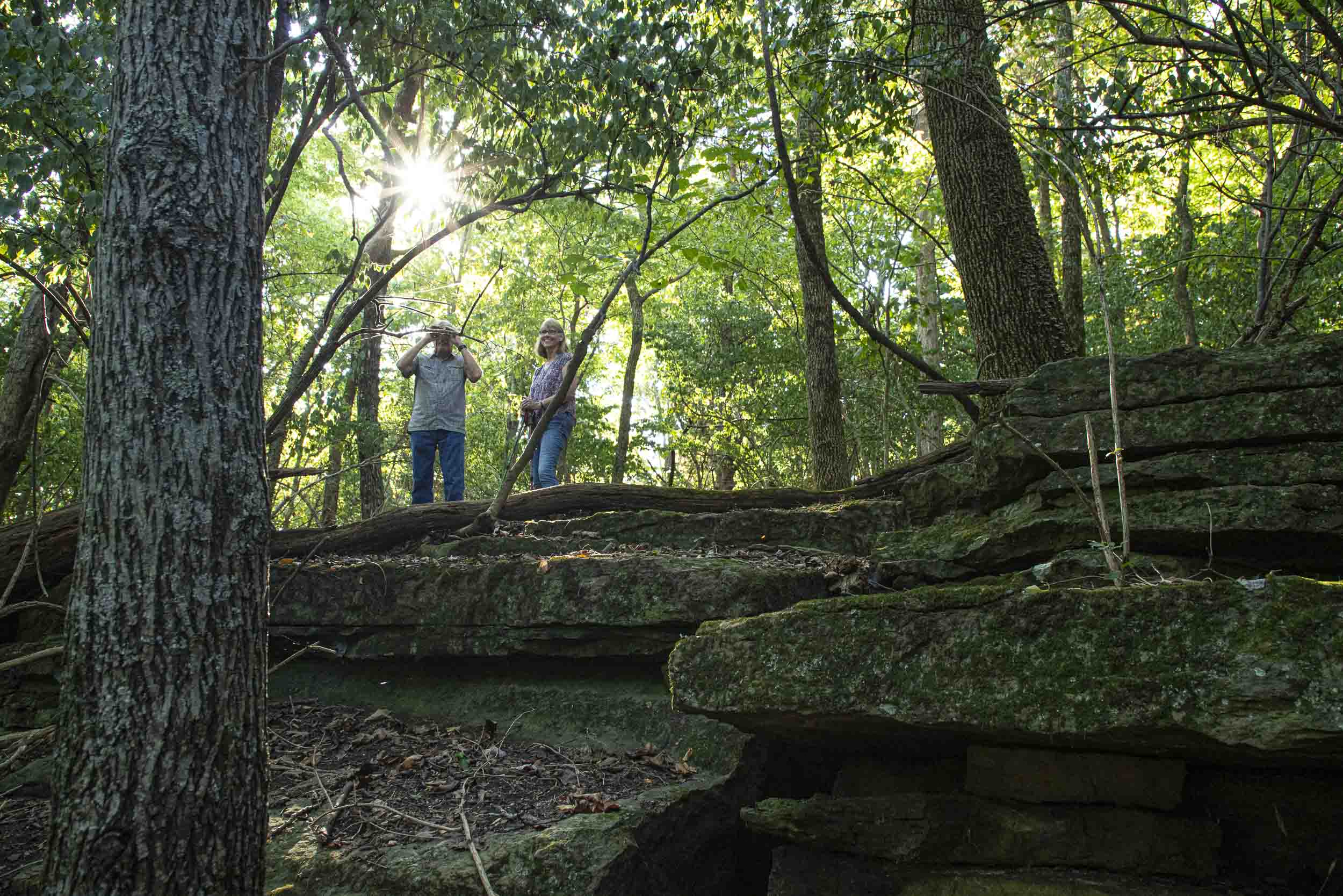 Two hikers stand above moss-covered rock shelves in a forest