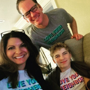 A man, woman and boy smile wearing Love Your Neighbor tee shirts