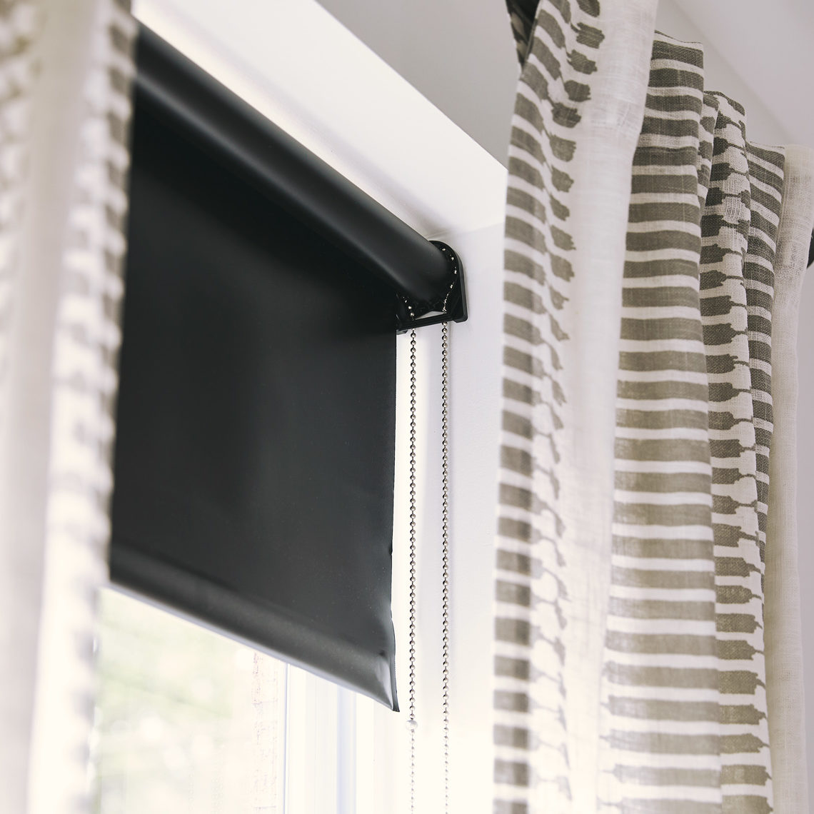 A blackout roller shade hangs between striped curtains