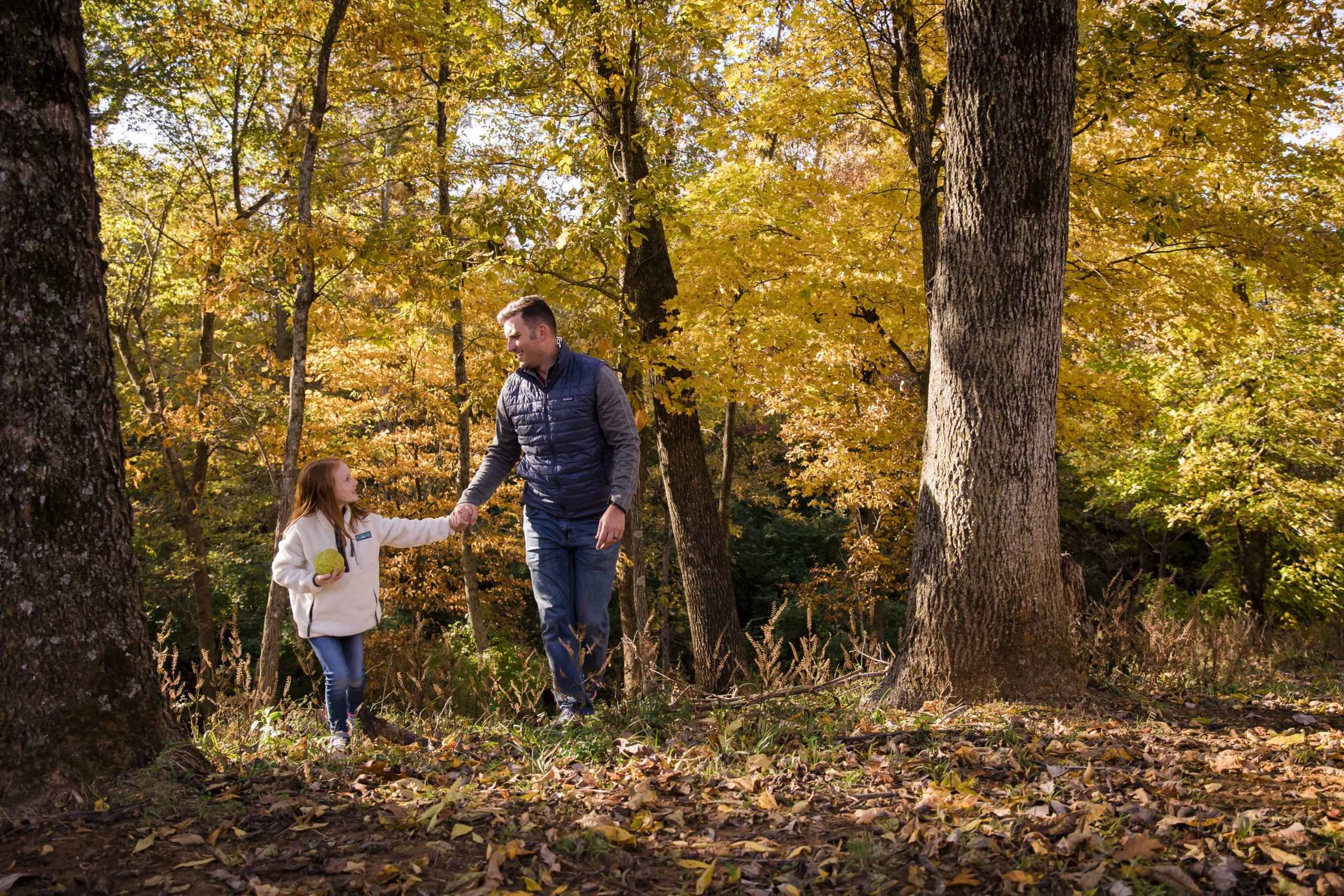A man and his daughter walk in a forest with yellow fall leaves